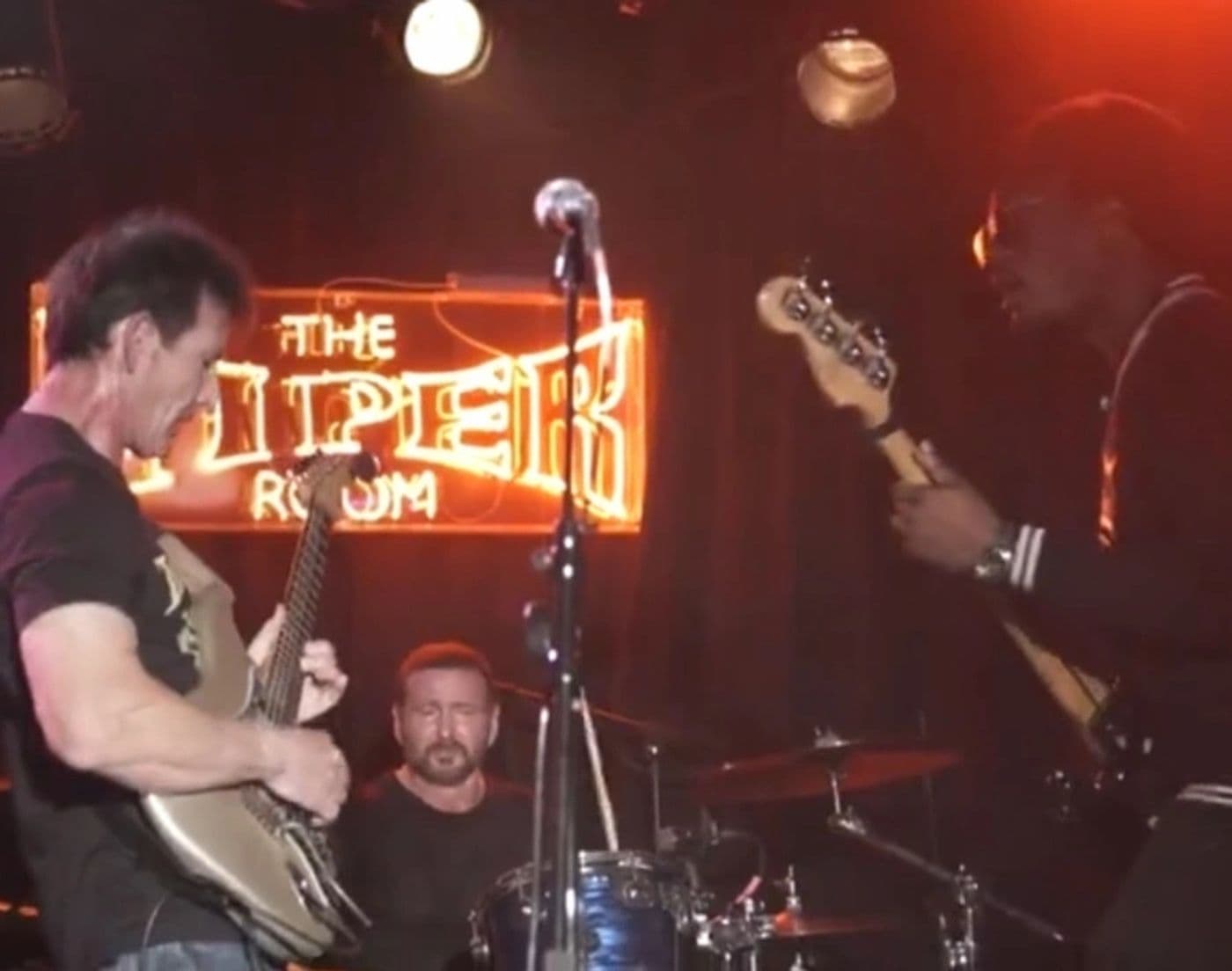 Guitarist and bassist facing each other on stage under the Viper Room neon sign
