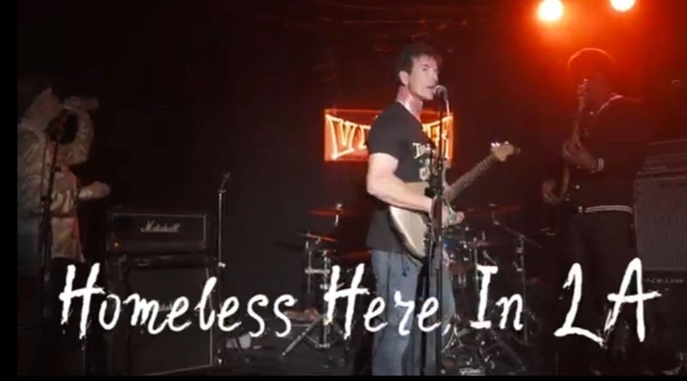 Live still from Homeless Here In LA, the band performing under red stage lights