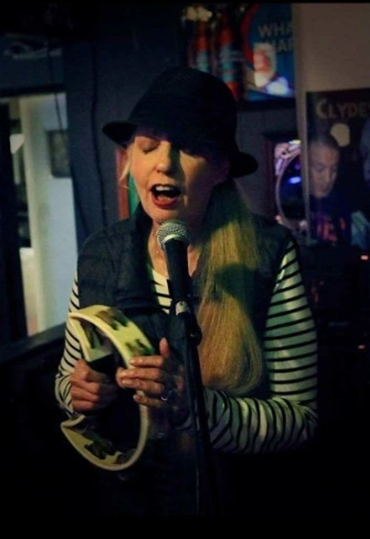 Clydescope singer in a black hat playing tambourine at the microphone